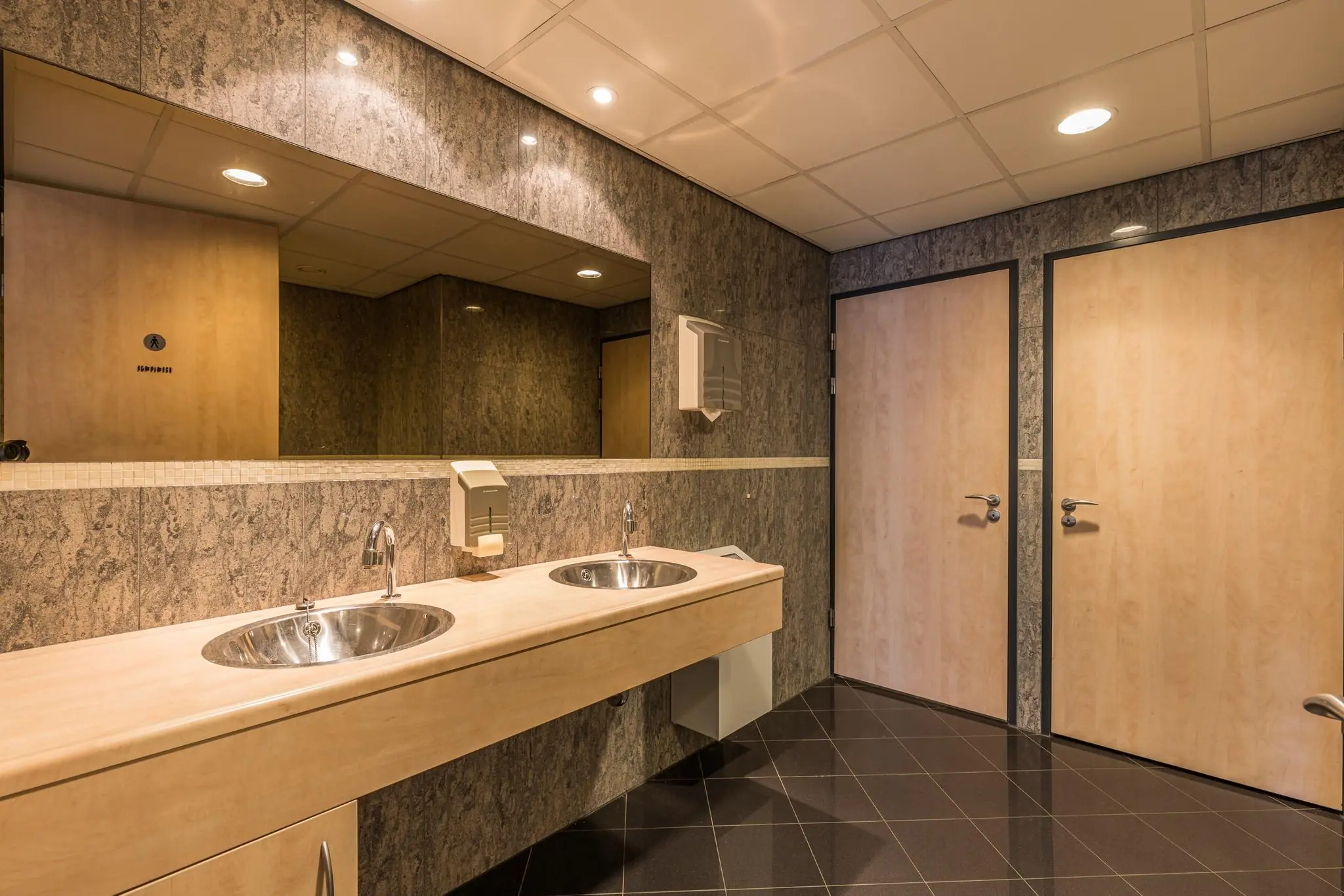 Moderne openbare toiletruimte met twee wasbakken, houten deuren en een grote spiegel aan de Laan Blussé van Oud-Alblas.